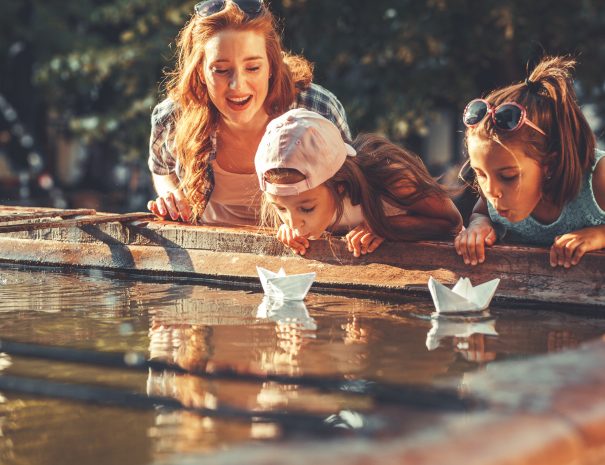 Mother and her daughters playing with paper boats in the fountai